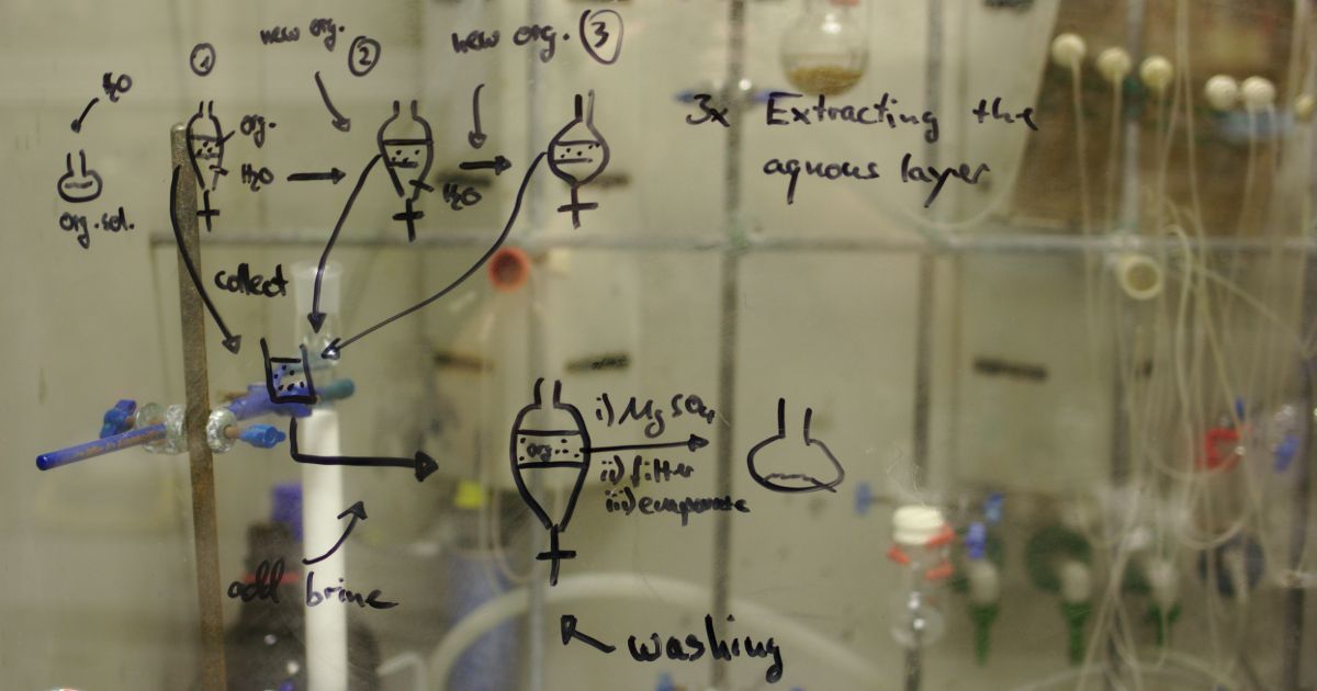 Hand-drawn chemical process diagram on glass with labeled flasks and arrows showing extraction steps.